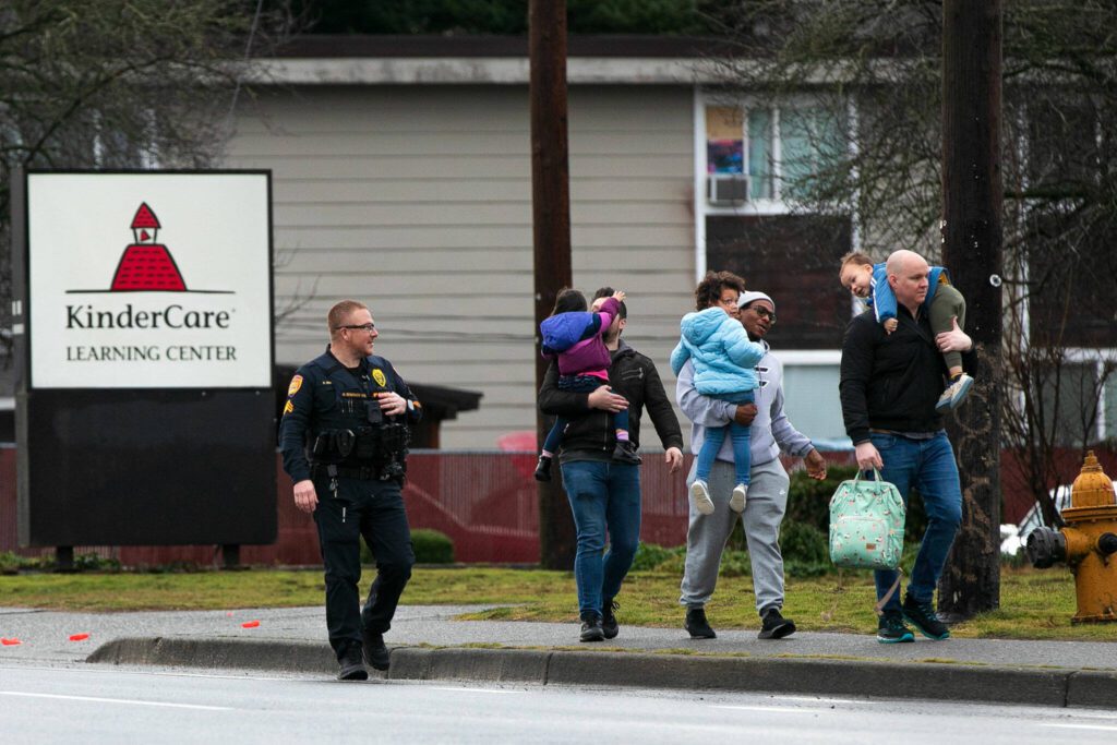 An officer escorts three parents with their children away from KinderCare after a shooting across the street at The Bluffs Apartments on Monday, Jan. 22, 2024, in Everett, Washington. Parents were able to get their children from the daycare center during the standoff. (Ryan Berry / The Herald) 