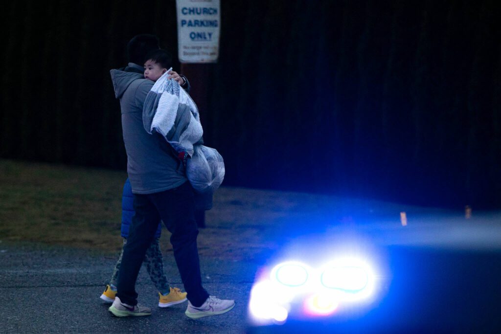 A parent leaves KinderCare with their child during a police standoff across West Casino Road at The Bluffs Apartments on Monday, Jan. 22, 2024, in Everett, Washington. (Ryan Berry / The Herald) 